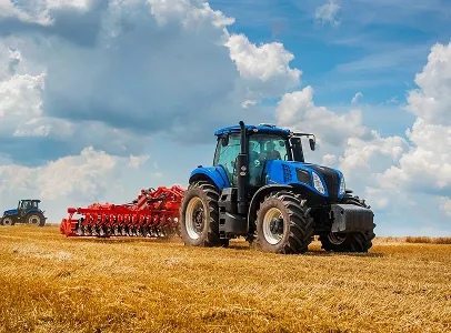 Tracteur bleu avec équipement rouge labourant un champ sec sous un ciel nuageux à Brûlon dans la Sarthe 72
