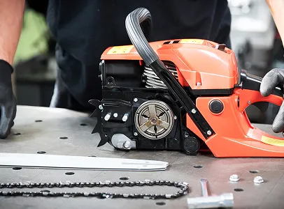 Tronçonneuse orange démontée sur une table, avec barre-guide, chaîne et outils à Brûlon dans la Sarthe 72