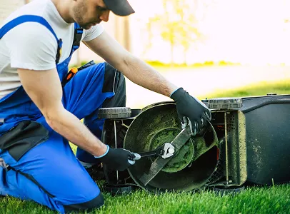 Un homme en salopette bleue et gants répare la lame d'une tondeuse à Brûlon dans la Sarthe 72
