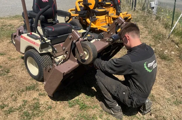 Un homme répare une tondeuse autoportée marron et beige sur de l'herbe sèche à Brûlon dans la Sarthe 72