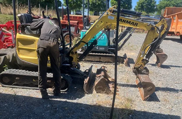 Homme en salopette réparant une mini-pelle Yanmar jaune avec godets de rechange à Brûlon dans la Sarthe 72