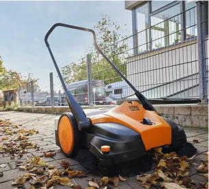 Un balai mécanique orange et noir balaye des feuilles mortes sur un trottoir à Brûlon dans la Sarthe 72