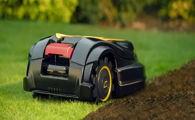 Robot tondeuse noir et jaune sur l'herbe verte coupée et la terre à Brûlon dans la Sarthe 72
